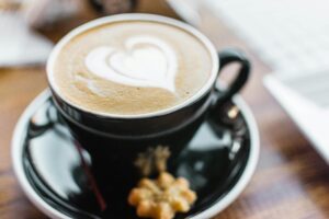 black ceramic cup with brown liquid with heart shape on black ceramic saucer