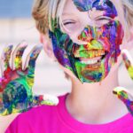 boy in pink crew neck top with paints on his hands and face