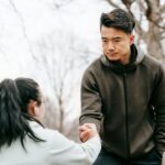 serious asian man giving hand to woman in park in daytime